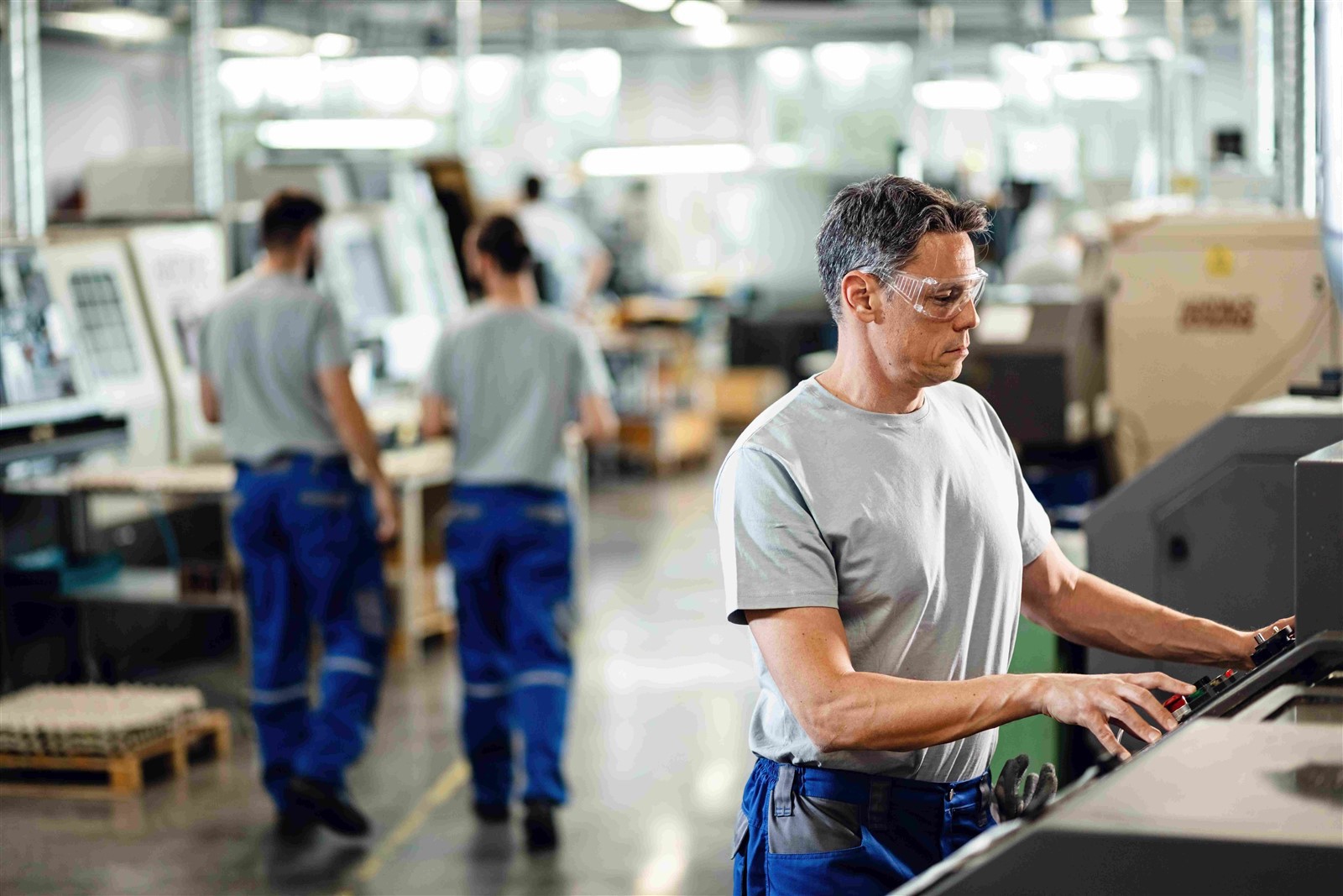 mid-adult-worker-operating-cnc-machine-while-working-industrial-facility mid-adult-worker-operating-cnc-machine-while-working-industrial-facility